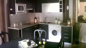 A compact kitchen with a microwave, sink, and washing machine. There is a dining table with a tray of fruit and a cup. - Country Cottage / Bilbao (Gordexola)