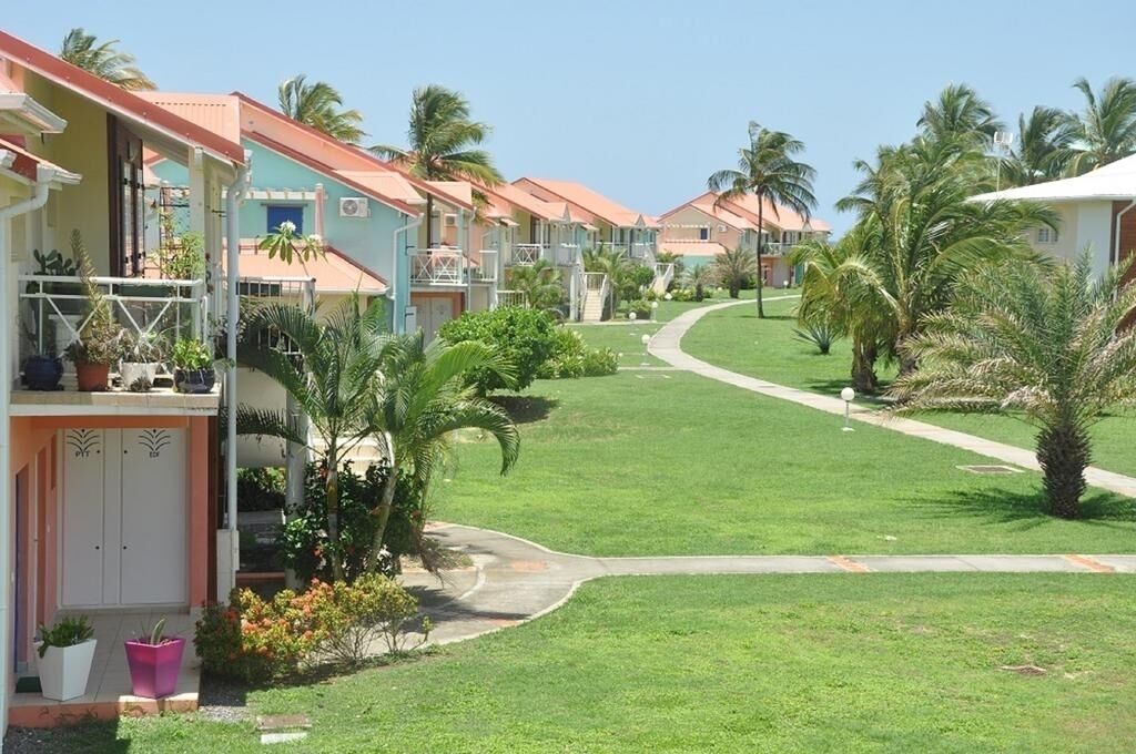 A row of pastel-colored buildings with balconies, surrounded by well-maintained lawns and palm trees.