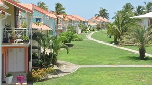 A row of pastel-colored buildings with balconies, surrounded by well-maintained lawns and palm trees. - Luxury residence on plage des raisins clairs in saint-francois (Saint-François)