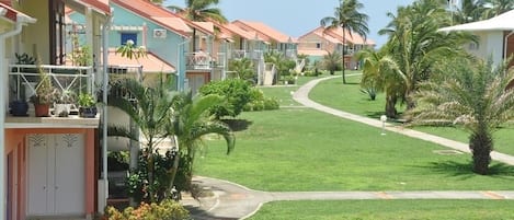 A row of pastel-colored buildings with balconies, surrounded by well-maintained lawns and palm trees.