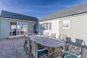 Eine überdachte Terrasse mit rundem Tisch und Stühlen, eine Glastür zum Zimmer und Blick auf das Meer.