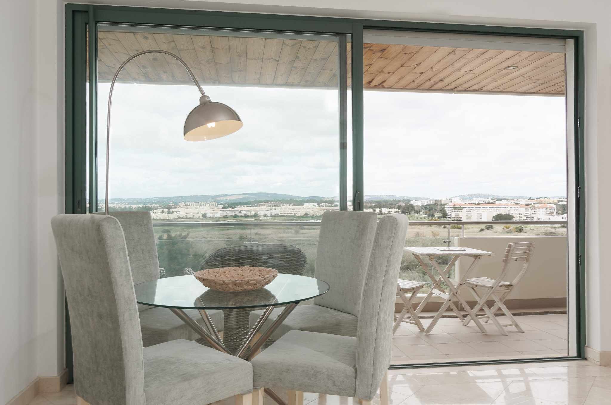Un balcone con un tavolo in vetro, due sedie e una lampada a sospensione.