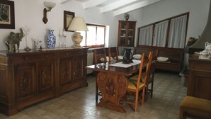 Zona pranzo con tavolo e sedie in legno, un mobile con vetrine e una finestra con tende.