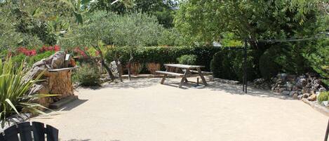 Un patio al aire libre con una mesa de picnic y sillas, rodeado de plantas y árboles.