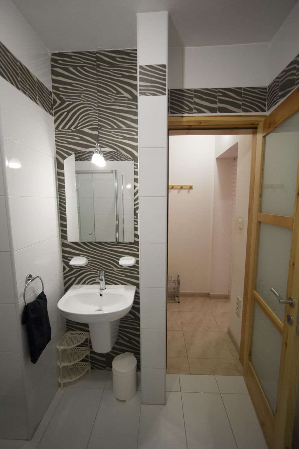 Un baño con una pared estampada con motivos de cebra, un lavabo blanco, un espejo y una puerta de madera.