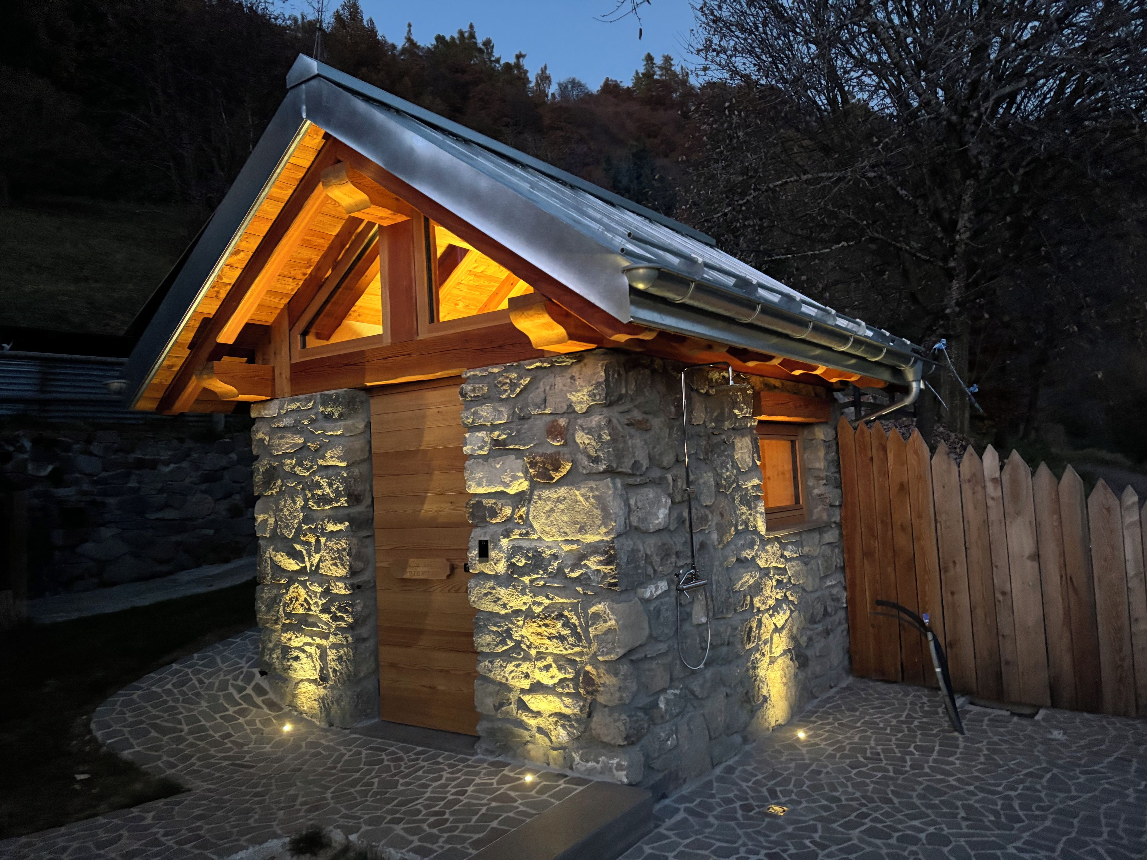 Eine Steinhütte mit Holztür, kleinem Fenster und Metallbedachung.