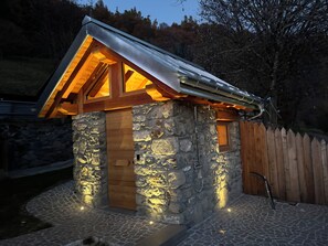 A stone cabin with a wooden door, a small window, and a metal roof. - Cozy Mountain Lodge (Roncegno Terme)