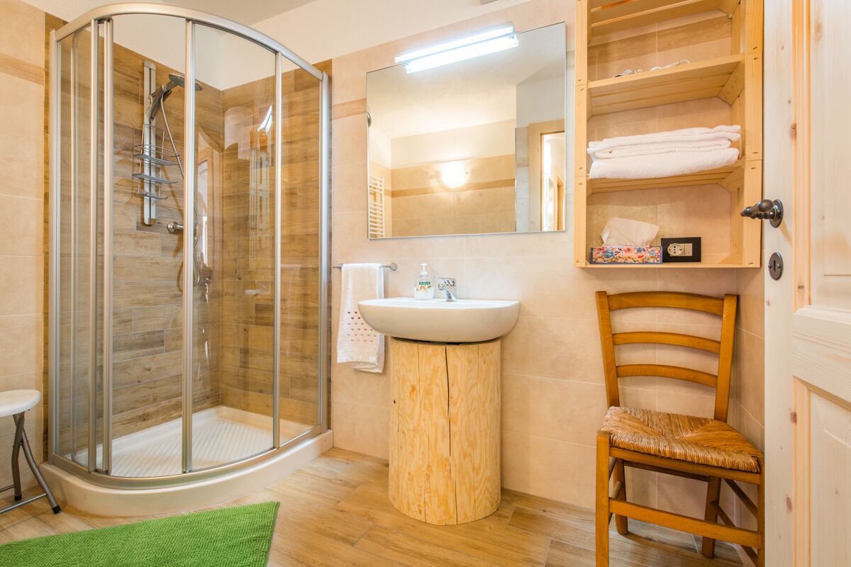 Ein Badezimmer mit einer Duschkabine, einem Waschbecken, einem Spiegel und einem Holzstuhl.
