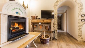 A cozy room with a fireplace, a television, and a stone archway. - Cozy Mountain Lodge (Roncegno Terme)