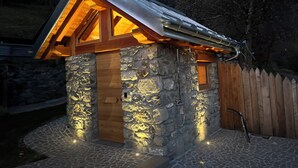 A stone cabin with a wooden door and a small window, surrounded by a wooden fence and a stone pathway. - Cozy Mountain Lodge (Roncegno Terme)