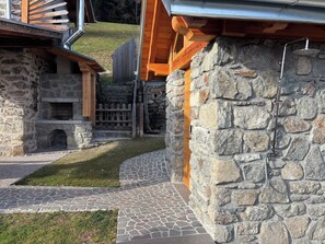 A stone building with a fireplace, a stone wall, and a metal shower. - Cozy Mountain Lodge (Roncegno Terme)