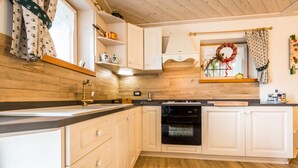 A kitchen with wooden flooring, white cabinetry, a black oven, and a window with a wreath decoration. - Cozy Mountain Lodge (Roncegno Terme)