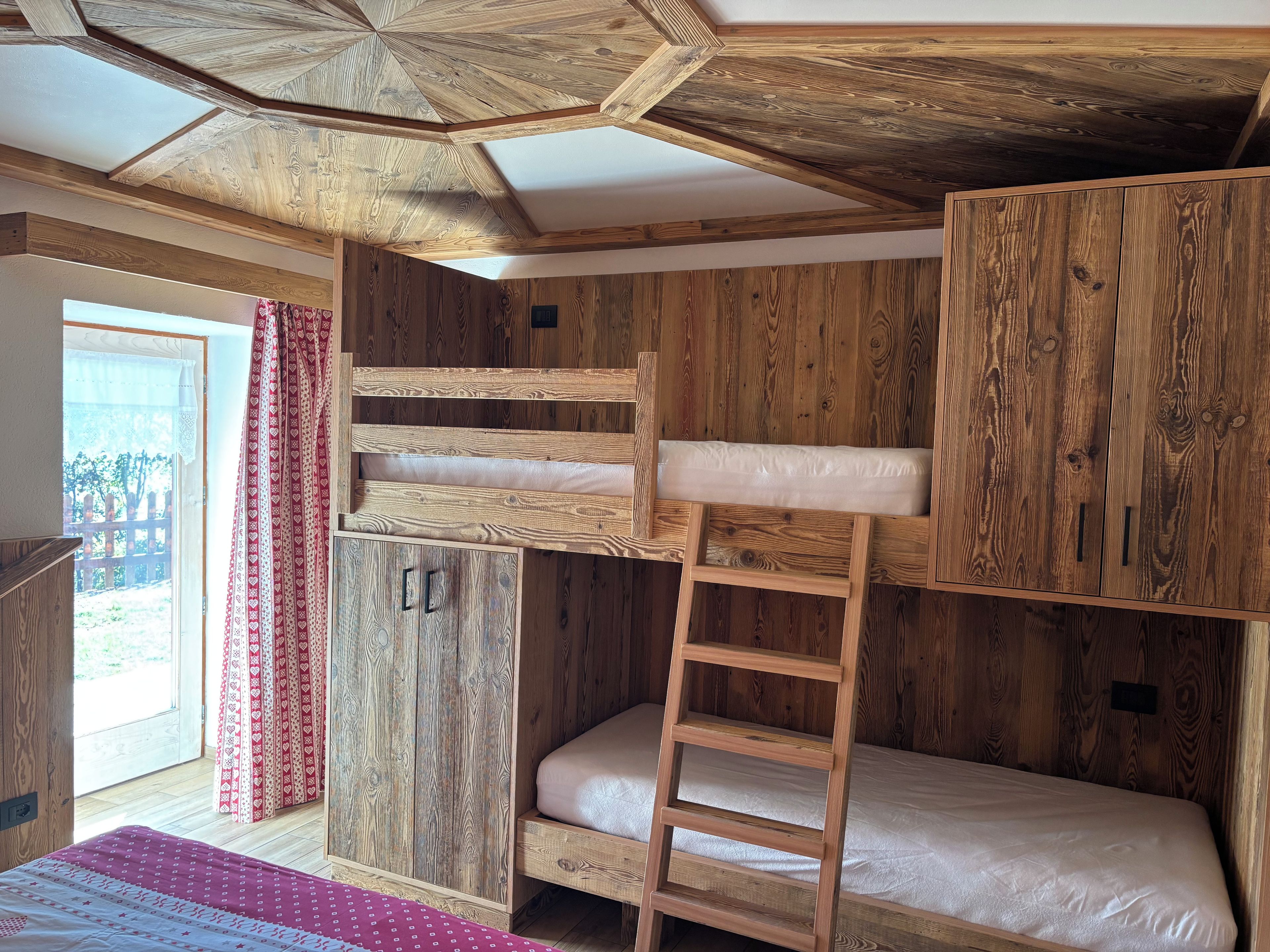 Ein Zimmer mit einem Etagenbett, Holzwänden, einer Leiter und einem Fenster mit Vorhängen.