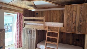 Une chambre avec un lit superposé, des murs en bois, une échelle et une fenêtre avec des rideaux.