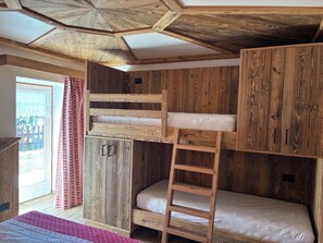 A room with a bunk bed, wooden walls, a ladder, and a window with curtains. - Cozy Mountain Lodge (Roncegno Terme)