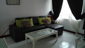 A living room with a dark-colored sofa, two green pillows, a glass-top coffee table, and a window with black curtains. - La Concha Beach. 2Dormitorios wifi and communal pools (Playa Honda)