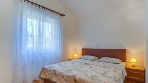 Une chambre à coucher avec un lit, deux lampes de chevet, une table de chevet en bois et une fenêtre avec des rideaux légers.