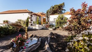 A house with a patio, surrounded by various plants and a wooden deck.