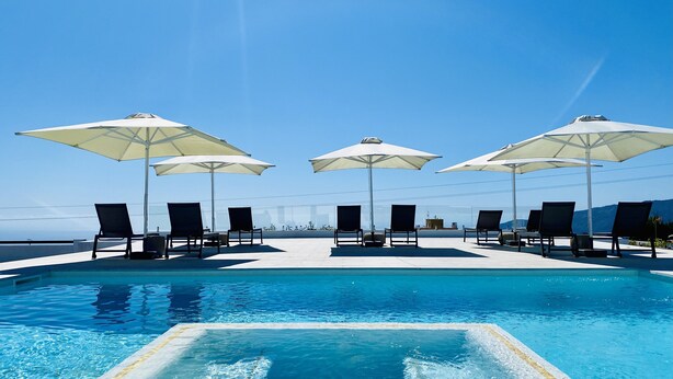 A poolside area with lounge chairs and umbrellas, overlooking a clear blue sky and distant landscape.
