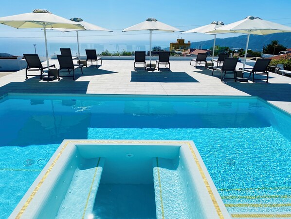 Una piscina con lettini e ombrelloni, cielo sereno e montagne in lontananza.