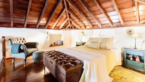 A bedroom with a wooden ceiling, a large bed, a chair, a nightstand, and a dresser.