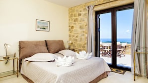 Camera da letto con parete in pietra, un letto con biancheria bianca e vista sul mare tramite una porta in vetro.