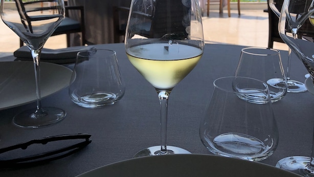 Une table avec un verre de vin blanc, des verres vides et une paire de lunettes de soleil.