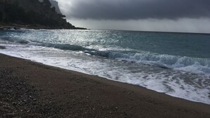 Une plage où les vagues se brisent sur le rivage, une falaise rocheuse en arrière-plan et un ciel nuageux.