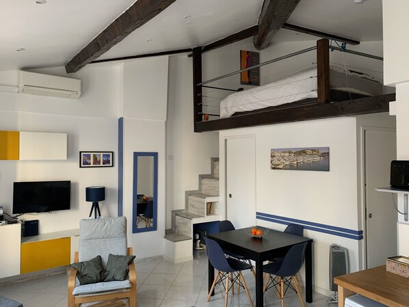 Un espace de vie compact comprenant une chambre en mezzanine, un coin repas et un coin salon.