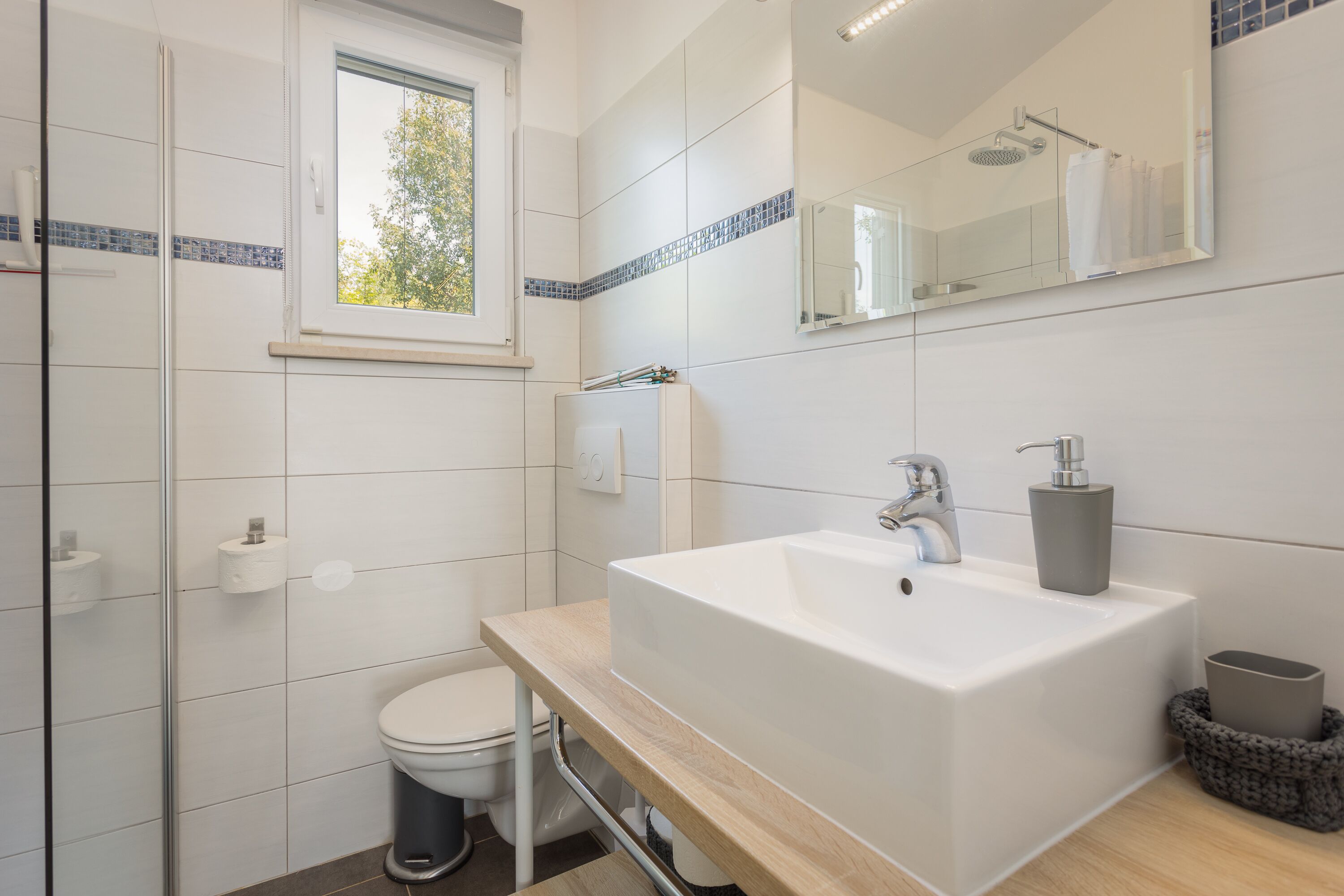 A modern bathroom with a white sink, mirror, and toilet.