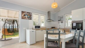 A modern kitchen with white cabinets, a built-in microwave, and an oven. There is a dining table with chairs and a hanging light fixture. - Beautiful house 20 meters from sea, free Wi-Fi (Peroj)