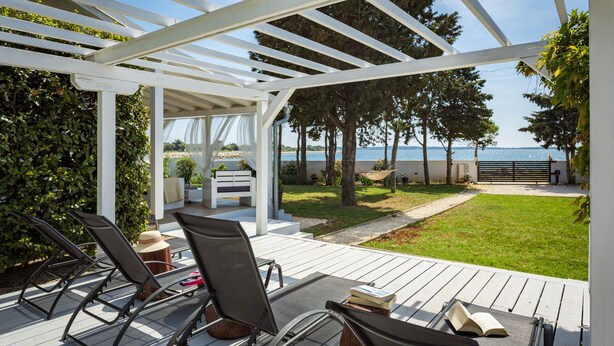 A covered outdoor seating area with chairs and tables, overlooking a grassy area and a body of water. - Beautiful house 20 meters from sea, free Wi-Fi (Peroj)