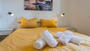 A neatly made bed with yellow bedding and white towels, a painting of a sunset on the wall, and bedside lamps. - Beautiful house 20 meters from sea, free Wi-Fi (Peroj)