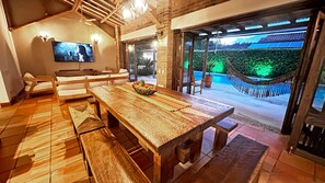 A wooden dining table with benches, a television mounted on the wall, and a view of a swimming pool with a hammock. - Fincas Panaca Jagüey 21 Grupo VIP | Exclusivity, swimming pool and heated Jacuzzi (Quimbaya)