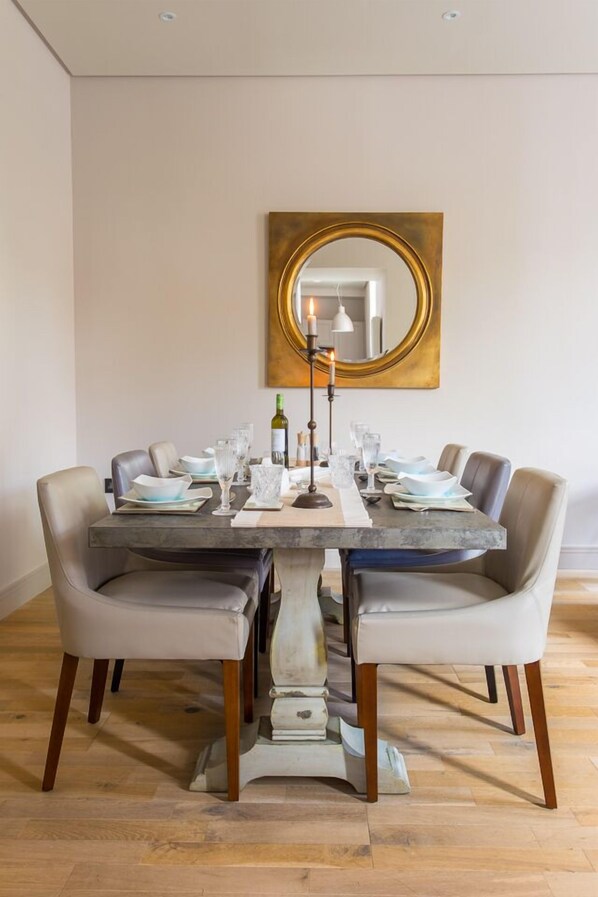 A dining table with six chairs, a centerpiece, and a large mirror on the wall.