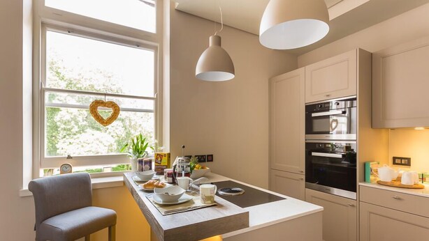 Una cocina moderna con una isla central, luces colgantes y un adorno con forma de corazón en la ventana.