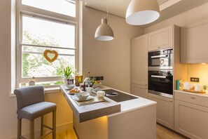 A modern kitchen with a central island, pendant lights, and a heart-shaped decoration on the window.