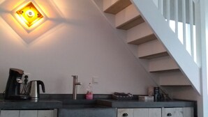 A kitchen with a built-in stove, sink, and cabinets. There is a staircase with wooden steps and white railings.