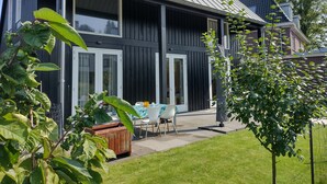 A modern two-story house with large windows, a covered patio, and a well-maintained lawn.