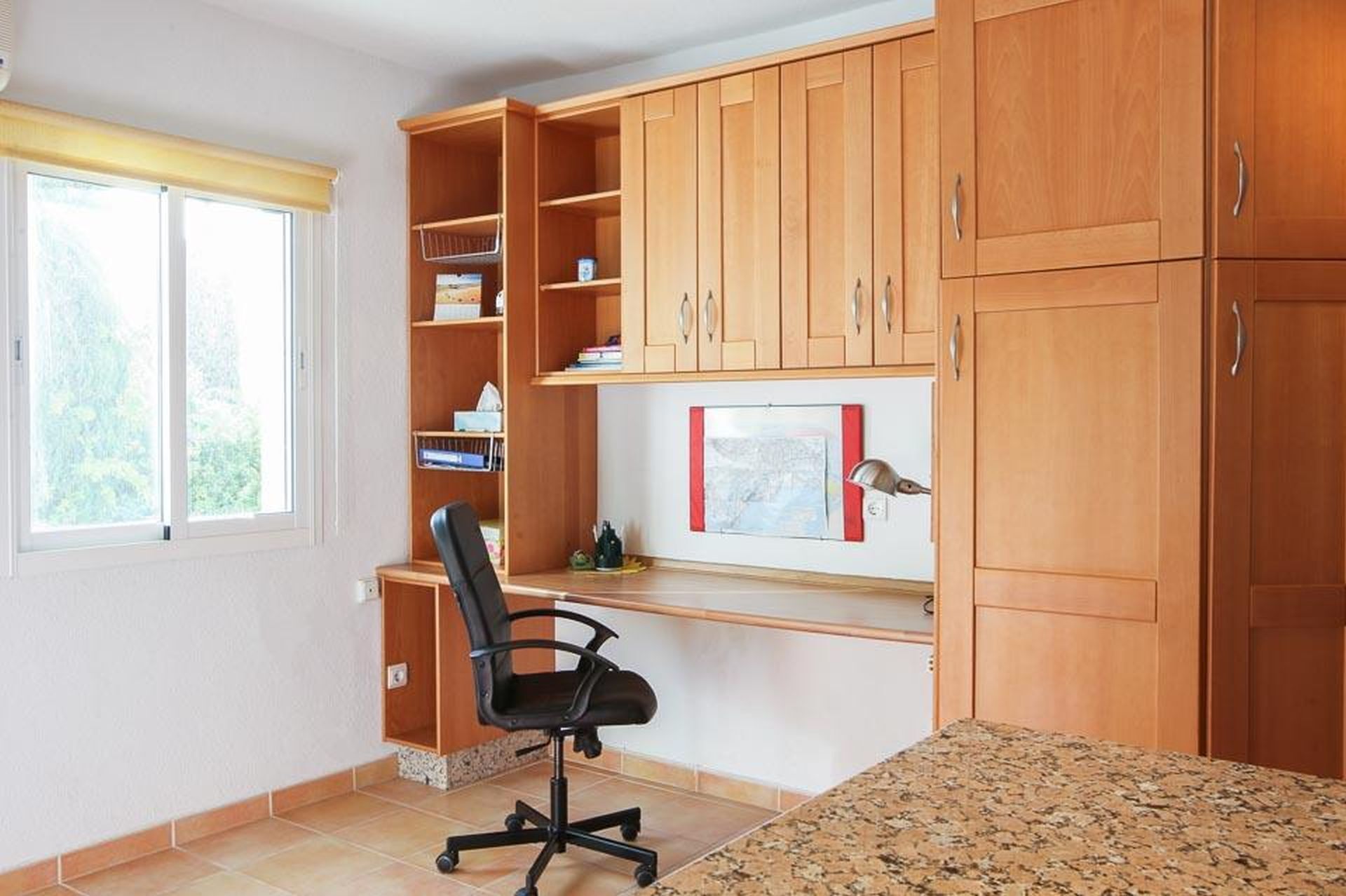 Ein Arbeitsraum mit Holzausstattung, einem Schreibtisch, einem Stuhl und einem Fenster.