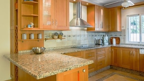 Een keuken met houten kastjes, granieten aanrechtbladen, een rvs afzuigkap en een raam dat voor natuurlijk licht zorgt.