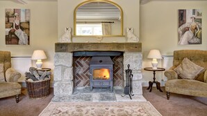 A cozy living room with a stone fireplace, two armchairs, a rug, and artwork on the walls.