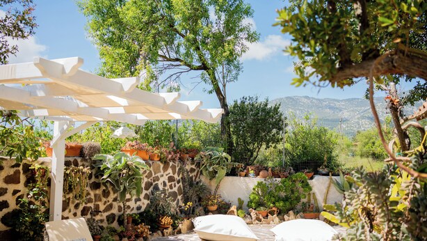 A patio with stone flooring, white cushions, and a pergola.