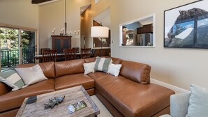 Ein geräumiges Wohnzimmer mit einem braunen Ledersofa, einem Couchtisch aus Holz und einem Essbereich mit Holzsesseln und einer Kandelaberleuchte.