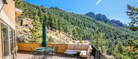 A wooden deck with outdoor furniture, including a table and chairs, overlooking a forested mountain.