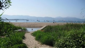 A beach path leading to a sandy beach with boats in the water and mountains in the background.