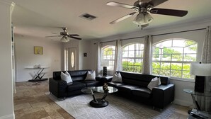 A spacious living room with a black leather sofa, a glass coffee table, and a ceiling fan. - Villagoona, waterfront, infinity pool, dir.access to the Gulf of America (Cape Coral)