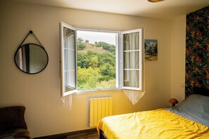 A bedroom with a bed, a window with curtains, a radiator, and a mirror on the wall.