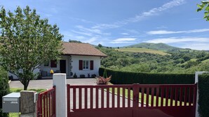 A gated property with a red gate, a white house with a red-tiled roof, and a lush green landscape in the background.