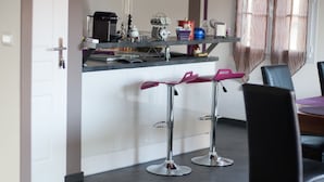 A modern kitchen with two bar stools, a dining table with chairs, and a window with curtains.